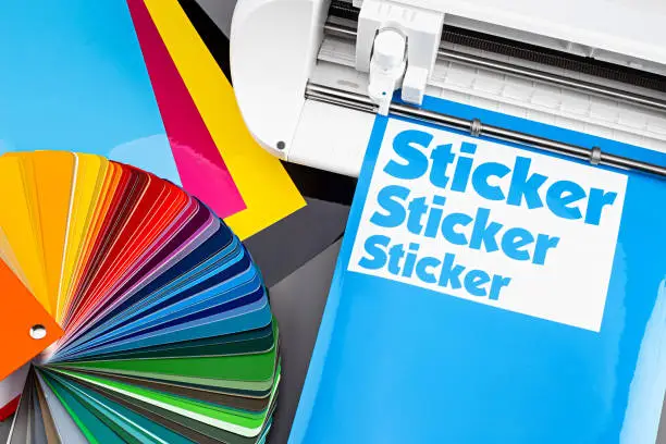 Photo of production making sticker with plotter cutting machine CMYK cyan blue colored vinyl fim with color fan. guide. Advertising Industry diy design concept background.