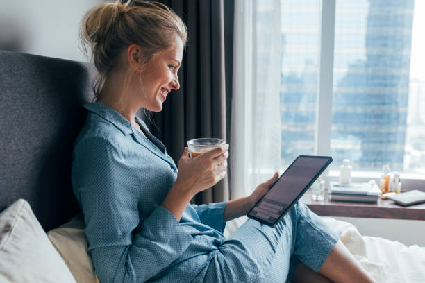 istock Happy Blonde Woman in Pajamas Writing E-mails on a Digital Tablet While Drinking Coffee in her Bedroom 1211550626
