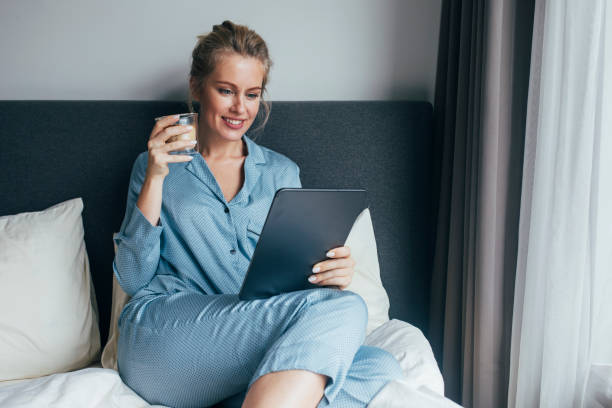 istock Planning Ahead: Smiling Blonde Woman Checking her Schedule for the Day on a Digital Tablet While Drinking Coffee in the Bedroom 1211550627
