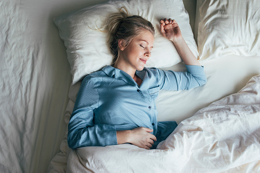 Beautiful happy Caucasian woman in blue pyjamas sleeping on a king-size bed.