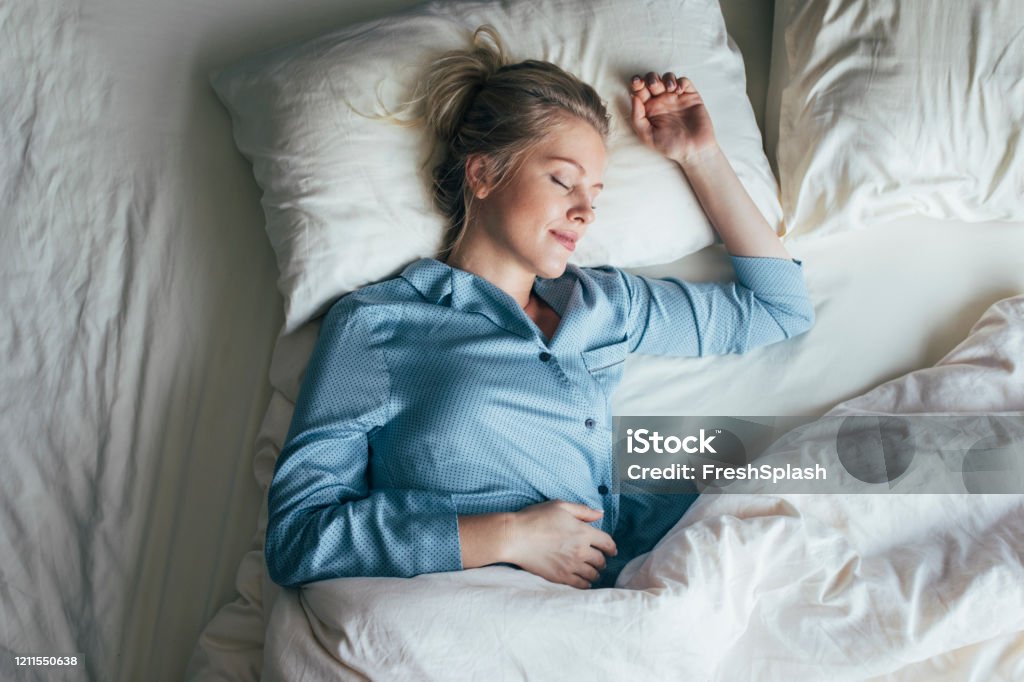 Sound Asleep: Overhead Waist Up Shot of a Pretty Blonde Woman in Blue Pyjamas Sleeping on a King Size Bed Beautiful happy Caucasian woman in blue pyjamas sleeping on a king-size bed. Sleeping Stock Photo
