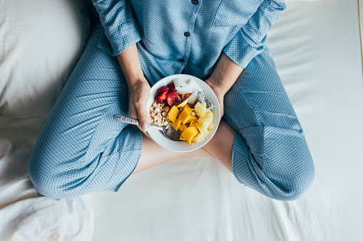Healthy morning routine: cropped image of a woman siting cross-legged and holding a bowl of delicious cereal with fruit.
