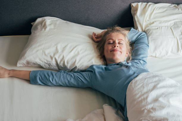 sensazione energizzata: la donna bionda felice in pigiama si allunga a letto dopo essersi svegliata al mattino - hotel room hotel bed bedroom foto e immagini stock