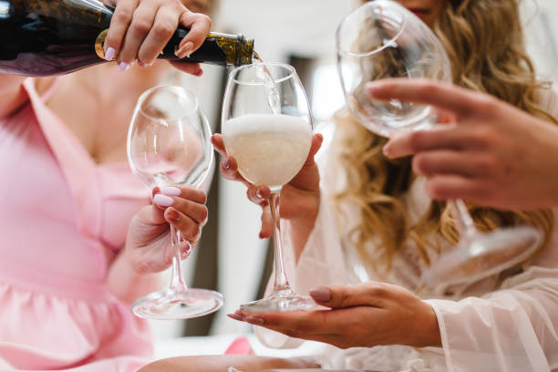 vierta el vino blanco. novia y damas de honor brindando con champán y divirtiéndose en la mañana de la boda. manos sosteniendo vidrio. foto de cerca de chicas celebrando una despedida de soltera. - drinking little girls women wine fotografías e imágenes de stock