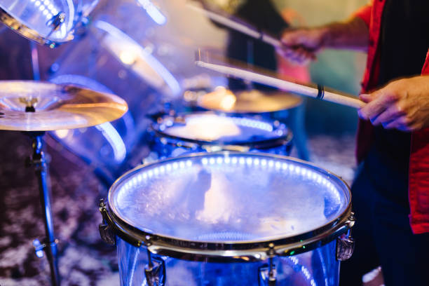 istock Man holding drum sticks, performing music. man plays musical percussion instrument on a black background. Drummer playing drum set at concert on stage. Music show. Bright scene lighting in club. 1211552792