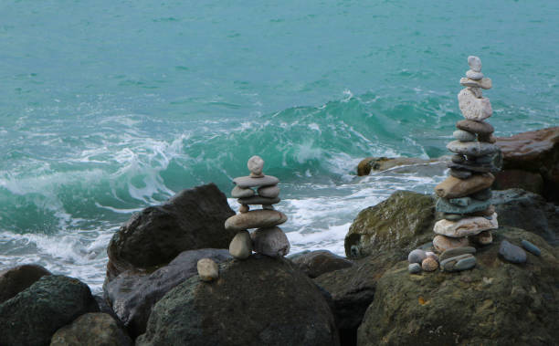 istock Stone cairn on seacoast in front of wave. Big rocks and balanced pebbles stack. Relaxation, harmony, balance concept. 1211552838