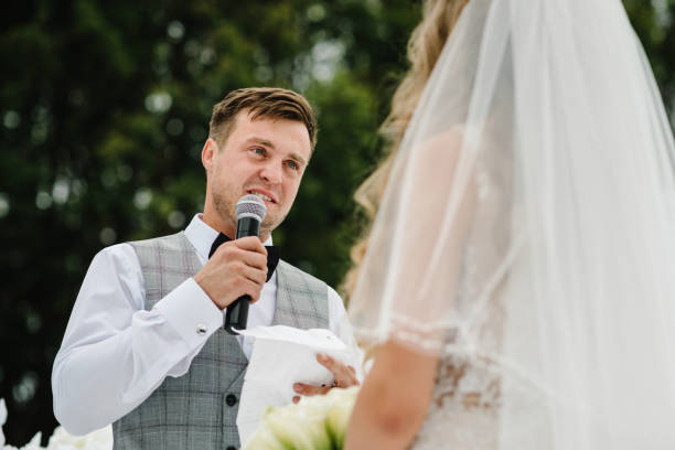 istock Happy bride and groom exchanging wedding vows on ceremony under the arch on the backyard banquet area. The groom says the promise in the microphone. Fidelity in love. 1211553050