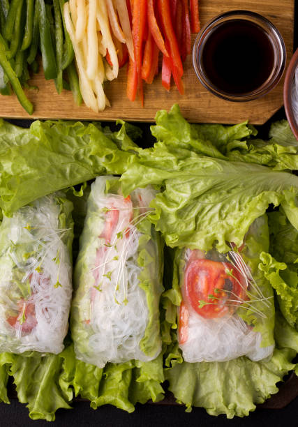 istock spring rolls with vegetables on a black background. Next to the ingredients are chopped peppers and soy sauce. 1211553359