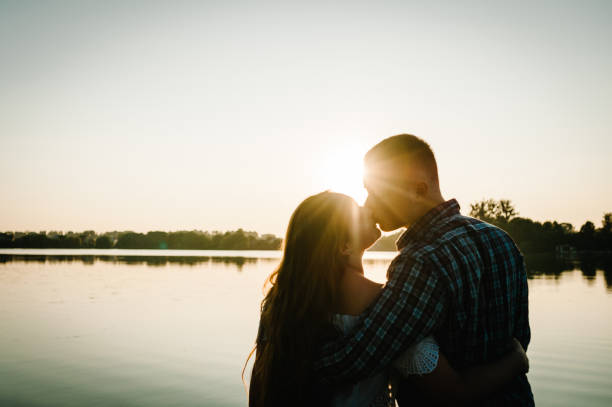 silueta de una pareja. pareja joven besándose y abrazándose al atardecer en primavera. un hombre y una mujer en el fondo del sol. concepto de amor y familia. de cerca. - silhouette kissing park sunset fotografías e imágenes de stock