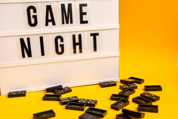 Game night text on lightbox with black dominoes on yellow background, table game, dominoes flying