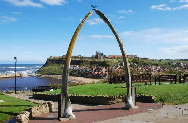 A whalebone arch at Whitby, North Yorkshire UK seen under a bright blue sky with Whitby Abbey visible on a distant headland seen through the arch.