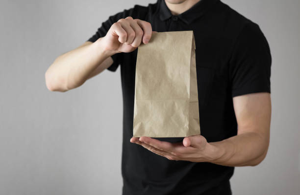 istock Man holds a paper bag. Close up. Isolated on a gray background 1211554832