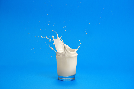 Close-up detail of a something dropping into a short glass of milk on the blue background