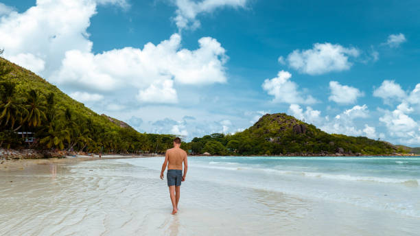 istock Praslin Seychelles,young men on tropical beach with palm tree, white beach man walking Seychelles Island, tanning men on tropical vacation 1211559084