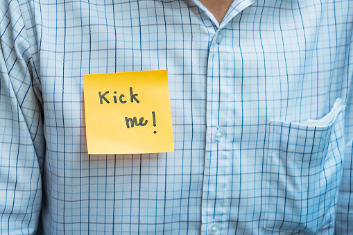 young man office with a yellow sticky note attached with the text Kick me. happy april fools day concept