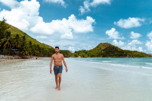 istock Praslin Seychelles,young men on tropical beach with palm tree, white beach man walking Seychelles Island, tanning men on tropical vacation 1211560232