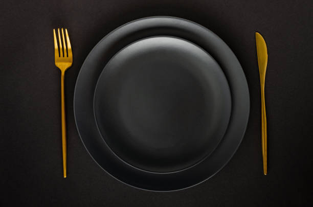 istock Black empty ceramic plate with golden cutlery (fork and knife) on a black background (table). 1211560628