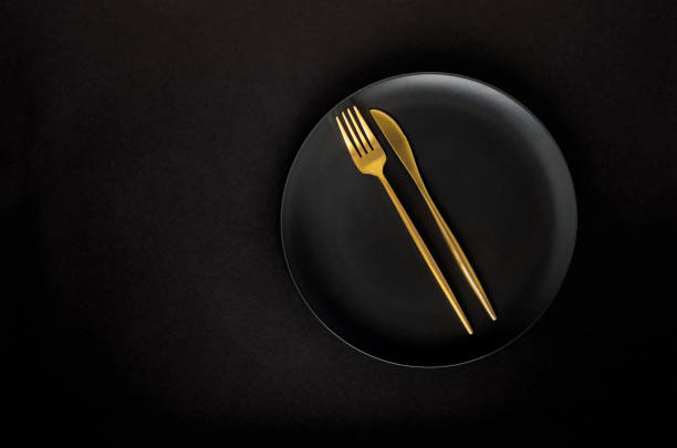 istock Black empty ceramic plate with golden cutlery (fork and knife) on a black background (table). 1211560671