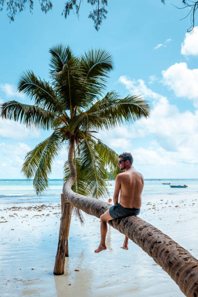 istock Praslin Seychelles,young men on tropical beach with palm tree, white beach man walking Seychelles Island, tanning men on tropical vacation 1211561377