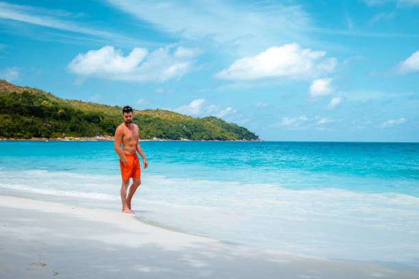 istock Praslin Seychelles,young men on tropical beach with palm tree, white beach man walking Seychelles Island, tanning men on tropical vacation 1211561531
