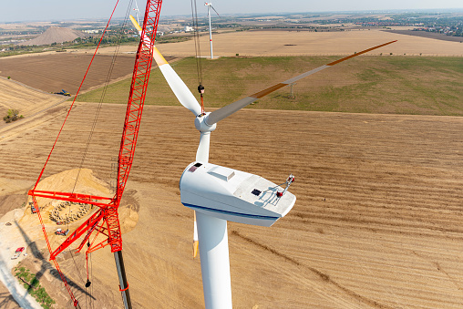 Large 1000 ton crane dismantles a wind turbine that is out of service on a sunny day with industrial climbers.