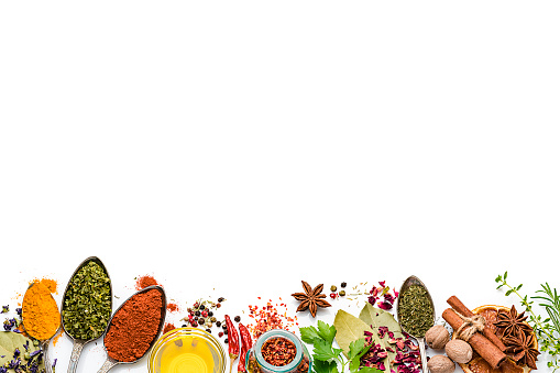 Cooking and seasoning backgrounds: Top view of multi colored vegetables, herbs and spices placed side by side at the bottom of a white background leaving useful copy space for text and/or logo. The composition includes rosemary, parsley, star anise, curry powder, bay leaves, nutmeg, salt, pepper, chili pepper, cinnamon sticks, dried orange slices, olive oil and dried oregano High key DSRL studio photo taken with Canon EOS 5D Mk II and Canon EF 100mm f/2.8L Macro IS USM.