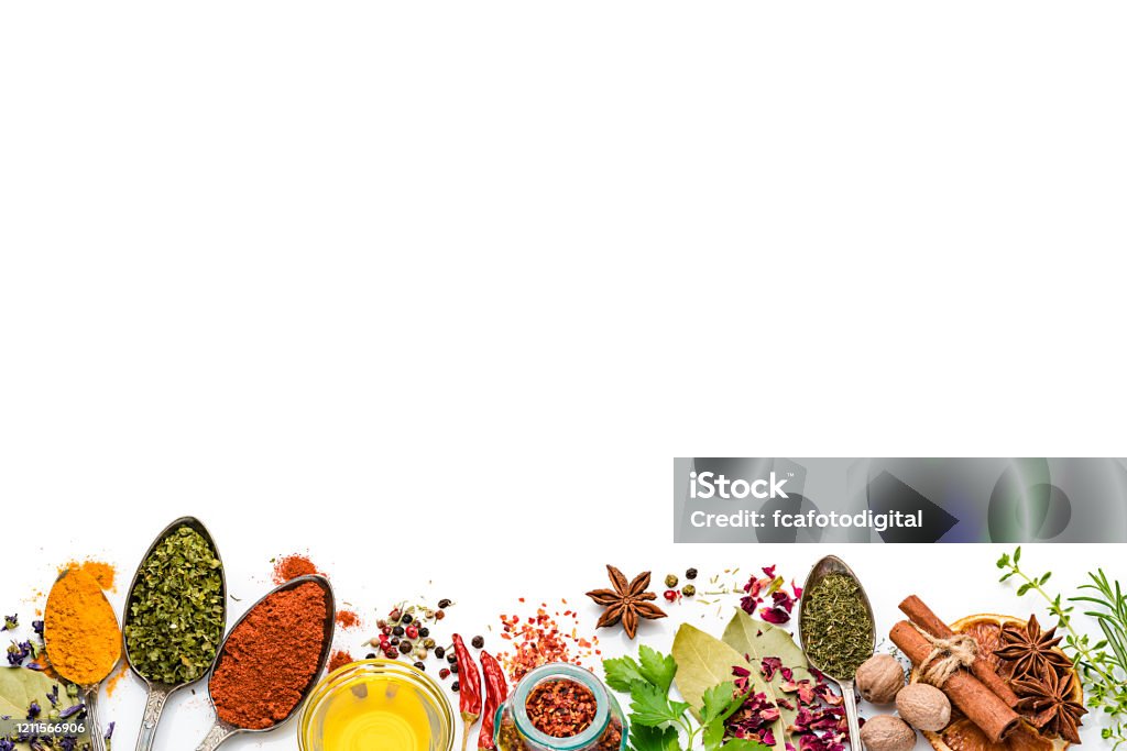 Vegetables, herbs and spices frame. Copy space Cooking and seasoning backgrounds: Top view of multi colored vegetables, herbs and spices placed side by side at the bottom of a white background leaving useful copy space for text and/or logo. The composition includes rosemary, parsley, star anise, curry powder, bay leaves, nutmeg, salt, pepper, chili pepper, cinnamon sticks, dried orange slices, olive oil and dried oregano High key DSRL studio photo taken with Canon EOS 5D Mk II and Canon EF 100mm f/2.8L Macro IS USM. Spice Stock Photo
