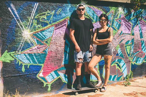 Portrait of a tattooed young couple in front of graffiti wall