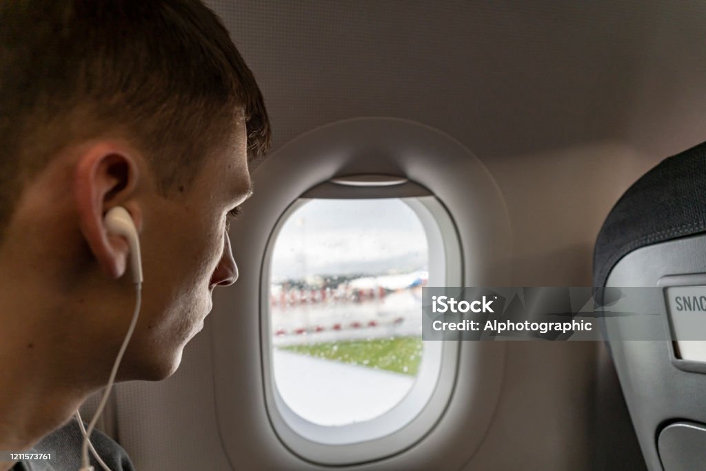 Young man looking out of plane window at Manchester airport Young man looking out of a rain soaked plane window at Manchester airport. Airplane Stock Photo