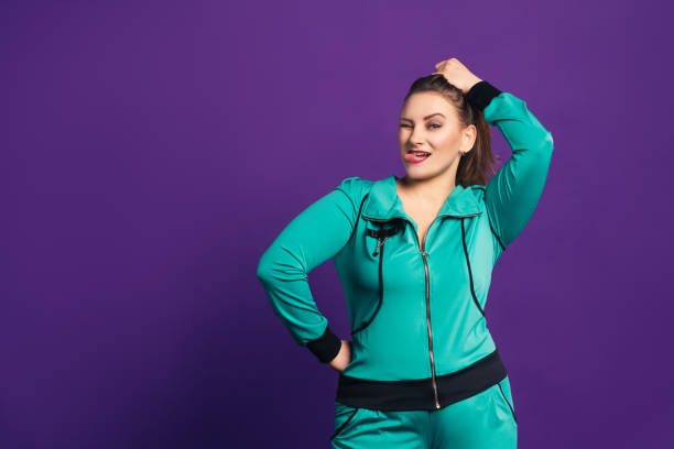 Funny plus size model in tracksuit shows her tongue, cheerful fat woman on purple background Funny plus size model in tracksuit shows her tongue, cheerful fat woman on purple background, body positive concept bizarre fashion stock pictures, royalty-free photos & images