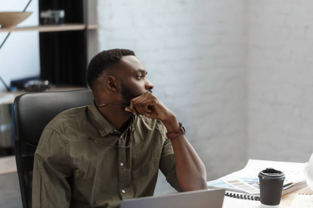 istock Afro-American architect working in office with blueprints.Engineer inspect architectural plan, sketching a construction project. Portrait of black handsome man sitting at workplace. Business concept 1211576992
