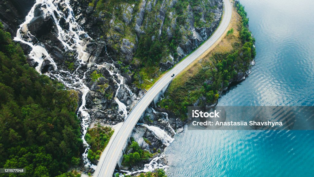 Vista aérea de la pintoresca carretera de montaña con coche, mar y cascada en Noruega - Foto de stock de Vía libre de derechos