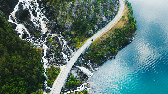 Aerial view of scenic mountain road with car, sea and waterfall in Norway