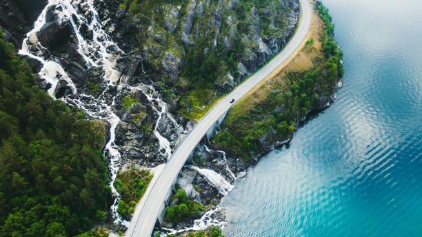 Aerial view of scenic mountain road with car, sea and waterfall in Norway Drone panoramic photo of the car driving through picturesque road above the huge waterfall near the fjord in South Norway norway photos stock pictures, royalty-free photos & images