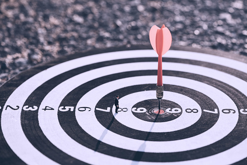 Businessman standing lookup red dart arrow hitting target centre dartboard on sunset background. Business targeting and focus.