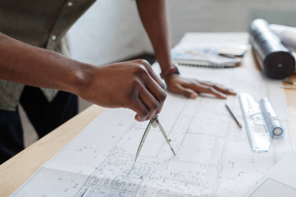 istock Afro-American architect working in office with blueprints.Engineer inspect architectural plan, sketching a construction project. Portrait of black handsome man sitting at workplace. Business concept 1211577836