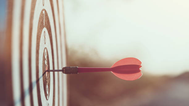 Close up red dart arrow hitting target center dartboard on sunset background. Business targeting and focus concept. Close up red dart arrow hitting target center dartboard on sunset background. Business targeting and focus concept. image focus technique stock pictures, royalty-free photos & images