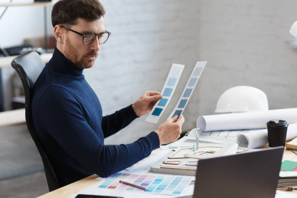 istock Architect working in office with color palette. Engineer select colors for building using color swatches, searching new ideas for construction project. Portrait of handsome bearded man at workplace 1211579298