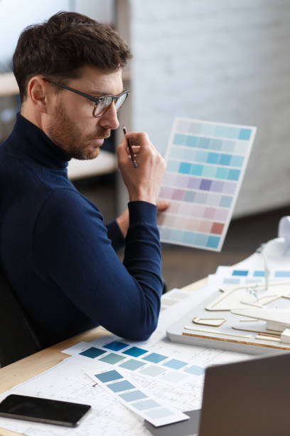 istock Architect working in office with color palette. Engineer select colors for building using color swatches, searching new ideas for construction project. Portrait of handsome bearded man at workplace 1211579341