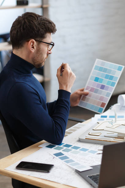 istock Architect working in office with color palette. Engineer select colors for building using color swatches, searching new ideas for construction project. Portrait of handsome bearded man at workplace 1211579529