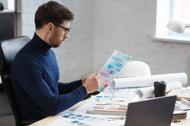 istock Architect working in office with color palette. Engineer select colors for building using color swatches, searching new ideas for construction project. Portrait of handsome bearded man at workplace 1211579554
