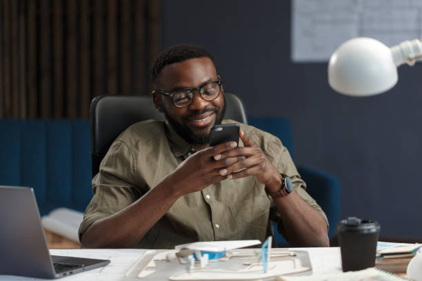 istock Young Afro-American man using smartphone and smiling. Happy businessman using mobile phone apps, texting message, browsing internet, looking at smartphone. Young people working with mobile devices 1211579588