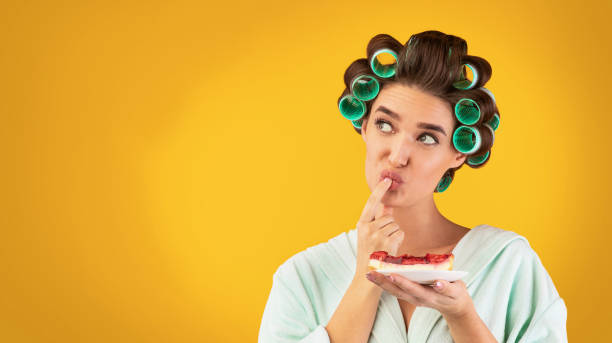 istock Hungry Housewife Tasting Cake Standing Over Yellow Studio Background, Panorama 1211579624