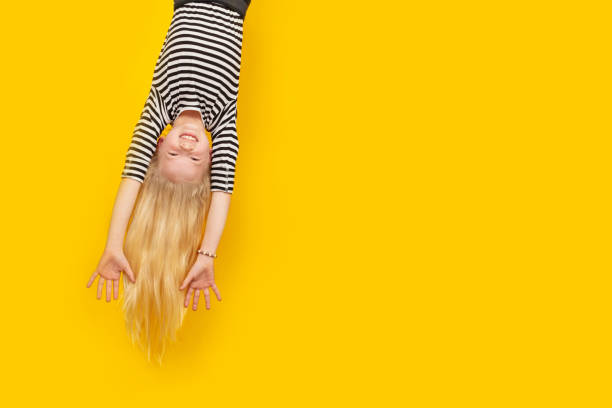 Excited crazy little blonde girl hanging happy upside down hands up over isolated yellow studio background. Emotion, expression. Copy space for text Excited crazy little blonde girl hanging happy upside down hands up over isolated yellow studio background. Emotion, expression. Copy space for text. upside down stock pictures, royalty-free photos & images
