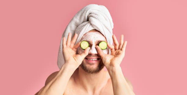 istock Guy with mask on face applies cucumber to eyes 1211579793