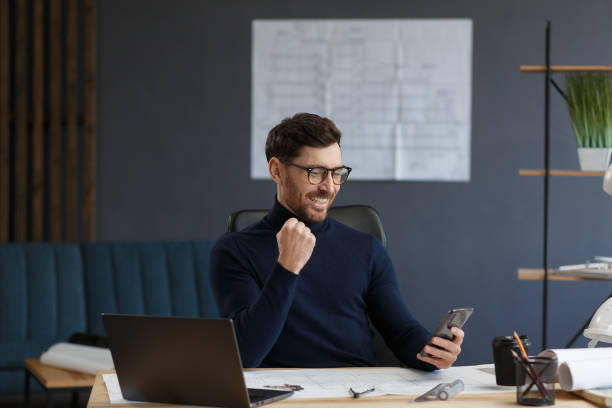 istock Young man using smartphone and smiling. Happy businessman using mobile phone apps, texting message, browsing internet, looking at smartphone. Concept of young people working with mobile devices 1211579898