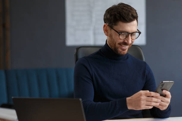 istock Young man using smartphone and smiling. Happy businessman using mobile phone apps, texting message, browsing internet, looking at smartphone. Concept of young people working with mobile devices 1211580219