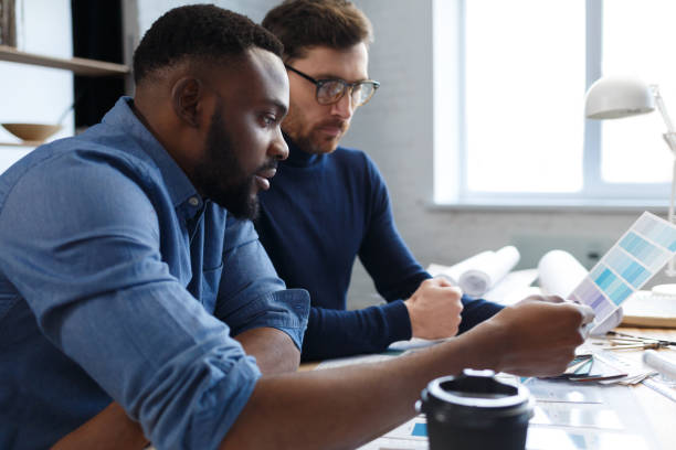 istock Multiracial engineer team working in office with color palette. Architects  select colors for building using color swatches, sketching and planning construction project. Partners discussing at work 1211581608