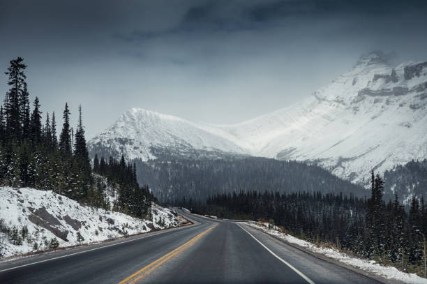 voyage panoramique sur la route avec la montagne de neige dans le sombre à icefields parkway - asphalt two lane highway natural phenomenon fog photos et images de collection