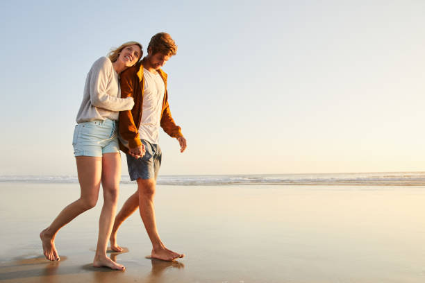 istock Young couple walking arm in arm together along a sandy beach 1211585932